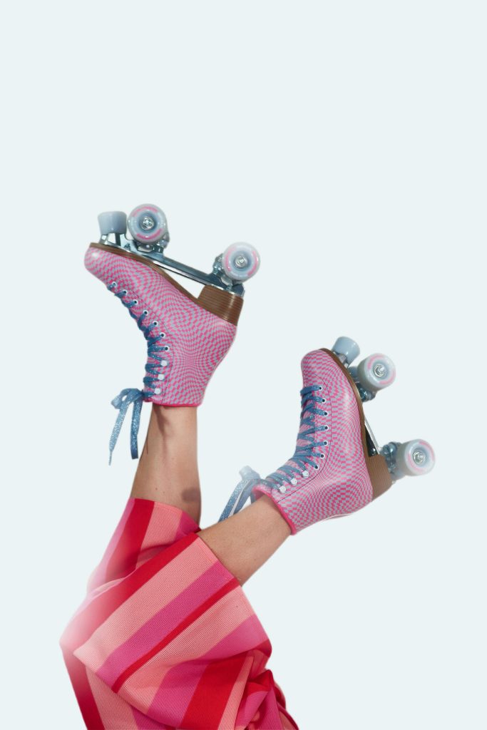 Vibrant pink roller skates with legs in red striped pants on a white backdrop.