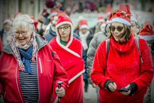 A joyful group participating in a festive Santa walk, wearing Santa hats and red attire.